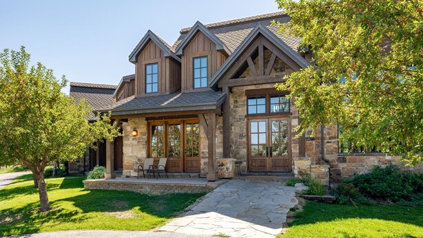 A large, two-story house with a stone facade, multiple windows, and a stone pathway leading to the entrance. - Rustic 8B Estate on 40 acres – 9,900sqft Estate on Private Ranch with 2 Hot Tubs (Heber City)