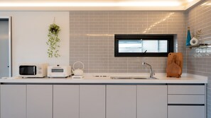 Une cuisine moderne équipée d’un four à micro-ondes, d’un grille-pain et d’une bouilloire sur le plan de travail, d’une plante suspendue et d’une fenêtre au-dessus de l’évier.
