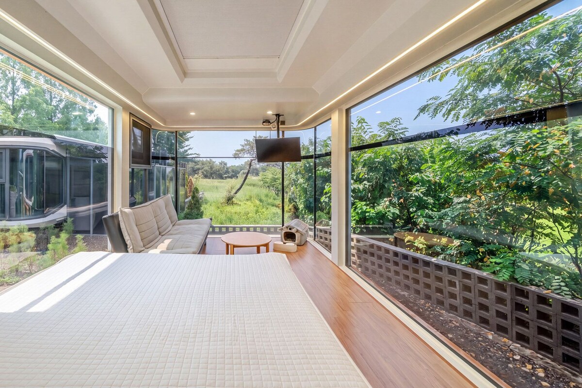 A bedroom with a large bed, a TV, and a view of a vehicle and greenery outside.