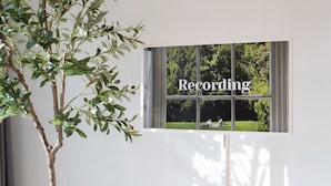 Una ventana instalada en la pared con vista a un parque y la palabra “Recording”.