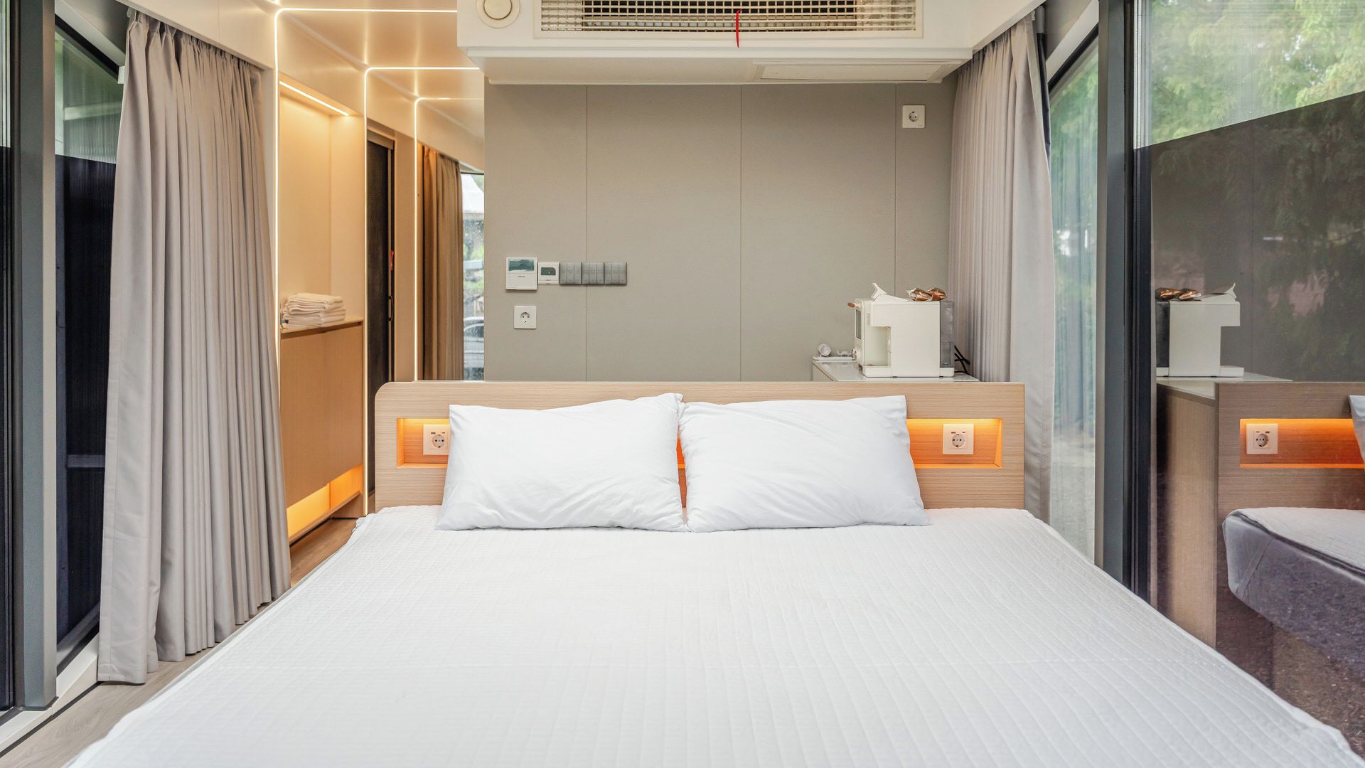 A modern hotel room with a large bed, bedside tables, a mirror, and a window with curtains.