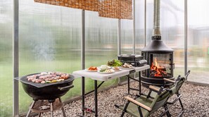 Een barbecue met eten, een tafel met borden, een draagbaar fornuis en een stoel.
