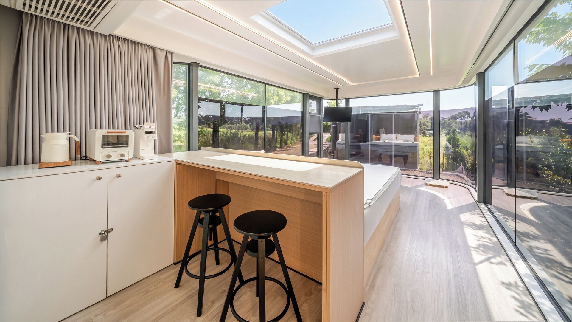 A modern kitchen with a central island, bar stools, and a view of the outdoors through large windows.