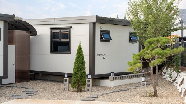 Un edificio moderno identificado como “THE ORION B2”, con un diseño minimalista, que presenta un ventanal y una puerta.