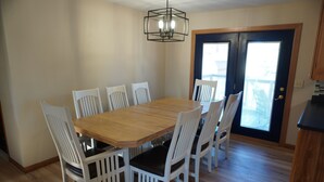 A dining area with a wooden table and white chairs, a black ceiling light, and a door with a window. - Charming 4-bedroom house with WiFi and gaming table in delightful Aberdeen (Aberdeen)