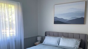 A bedroom with a bed, a nightstand, a lamp, a painting, and sheer curtains. - Country Cottage with Valley Views, 15mins to Canungra, 30mins to Mt Tamborine (Illinbah)