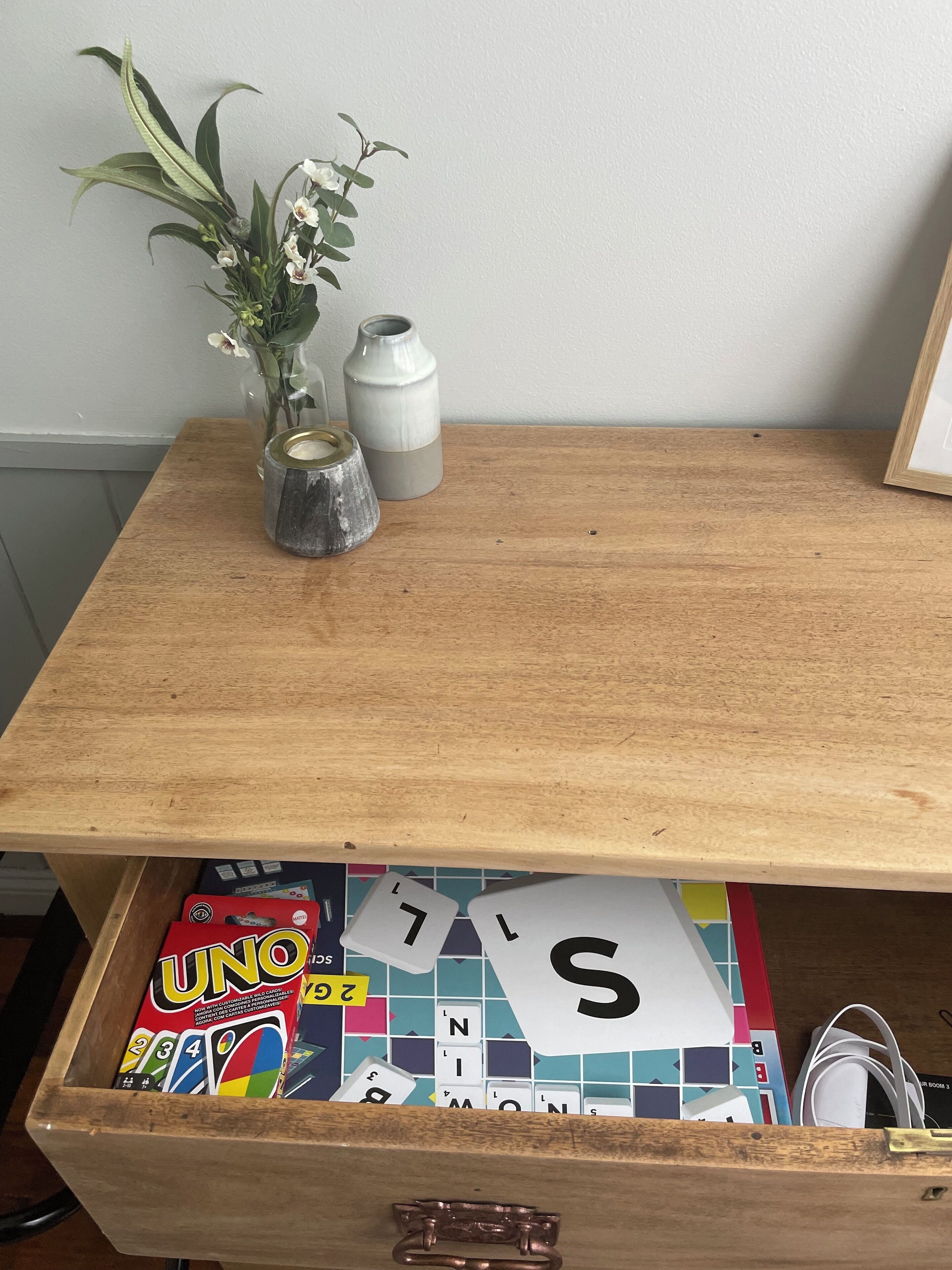 A wooden table with a drawer containing a board game and a vase with flowers.