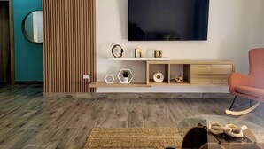 Una sala de estar moderna con un televisor de pantalla plana montado en la pared, una consola de madera con adornos, un sillón mecedora y una alfombra tejida en el suelo.