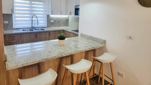 Una cocina moderna con encimera de granito, armarios de madera, horno empotrado y ventana con persianas.