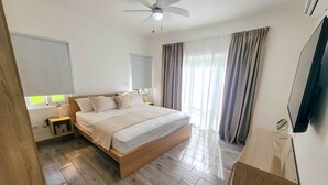 Un dormitorio moderno con cama de madera, mesita de noche, ventilador de techo y un gran ventanal con cortinas.