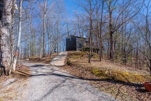 Escape to a secluded cabin surrounded by a tranquil forest, featuring a traditional heating system and a gravel driveway.