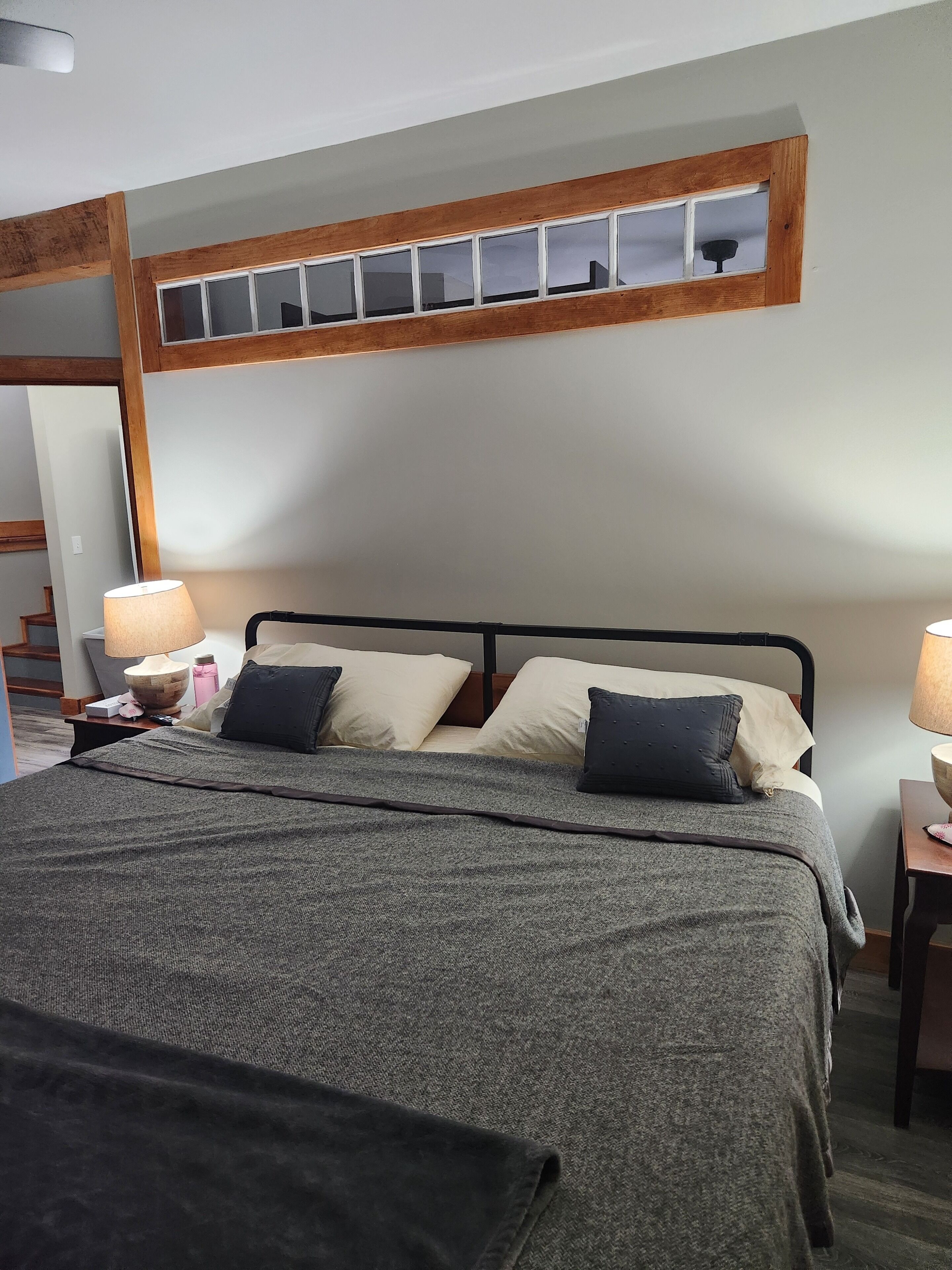 Une chambre à coucher comprenant un lit, deux tables de chevet, une tête de lit en bois et une fenêtre à carreaux.