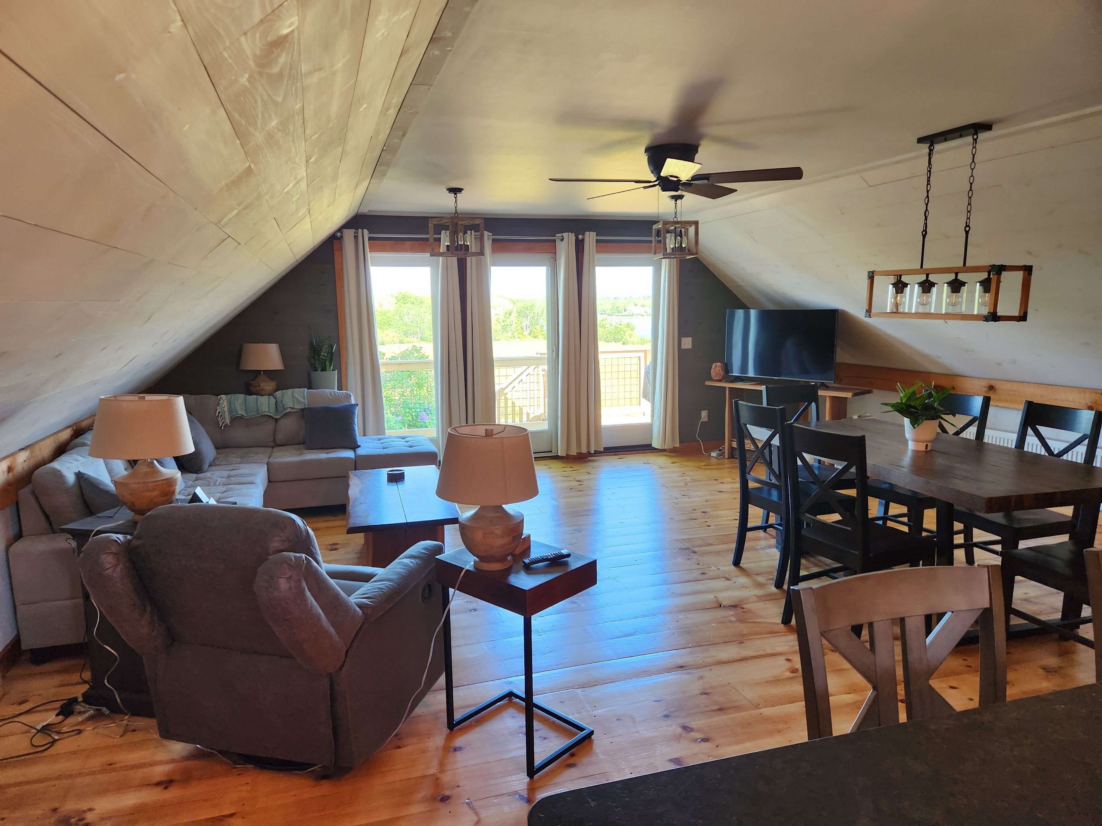 An attic-style living room with a sofa, armchair, dining table, and ceiling fan.