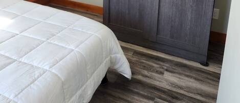 A bedroom with a bed, wooden beams, a grey wardrobe, and a white quilted bedspread.