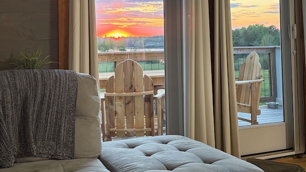 Una sala de estar acogedora con un gran ventanal, un sofá con cojines y una silla de madera.