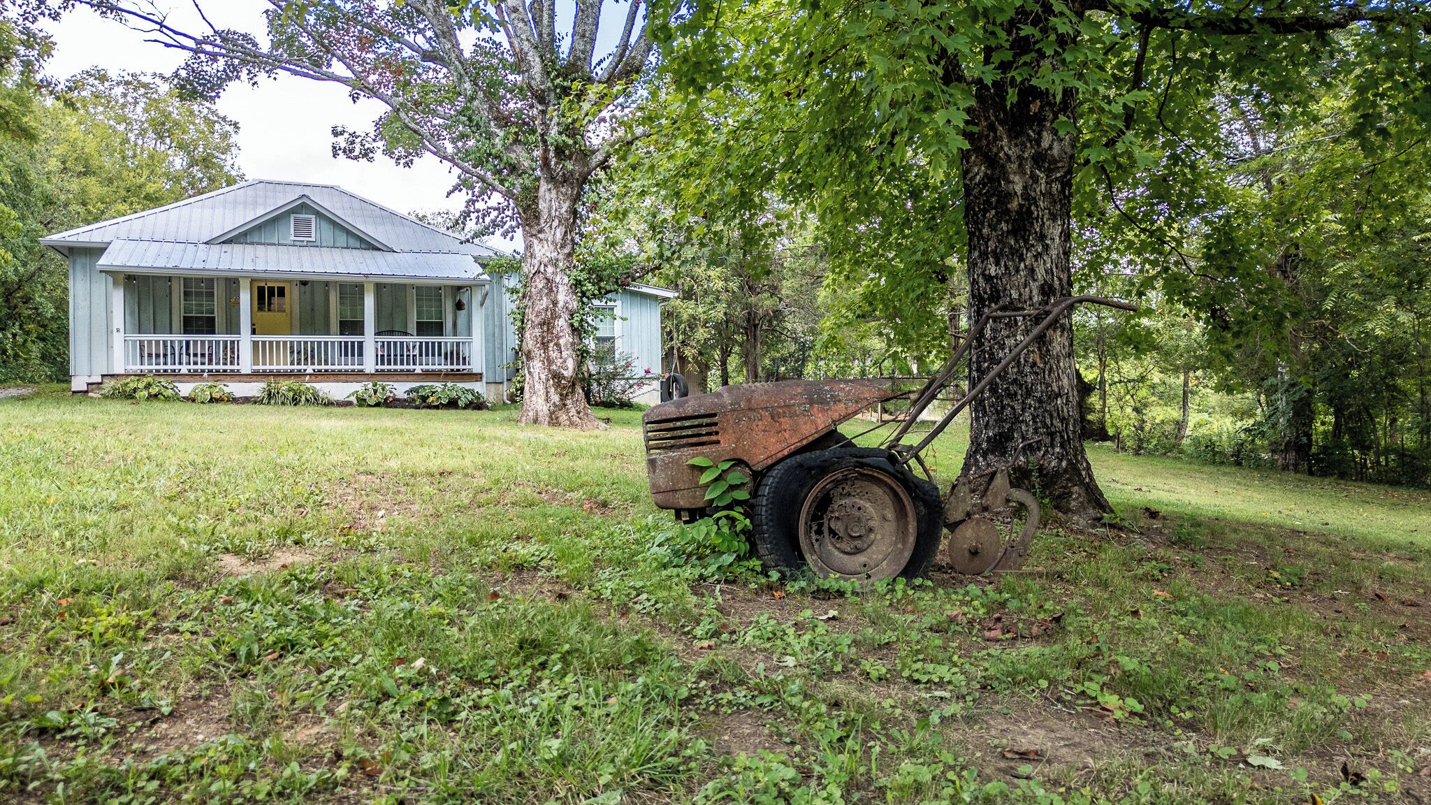 A rustic house with a porch, surrounded by a grassy yard and trees.
