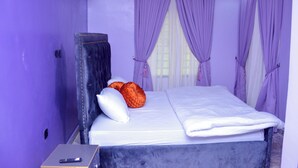 Un dormitorio con cama, cabecera y cortinas moradas.