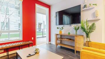 A living room with a red wall, a large flat-screen TV, a bench, a coffee table, and a yellow sofa.