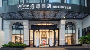 Het uiterlijk van UrCove by Hyatt, met een moderne gevel, grote glasramen, een opvallende ingang met een decoratieve boog en een dakbostuin.