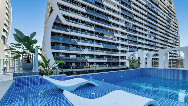 Een modern hotel met een groot zwembadgedeelte, voorzien van blauw betegelde vloeren en witte ligbedden.
