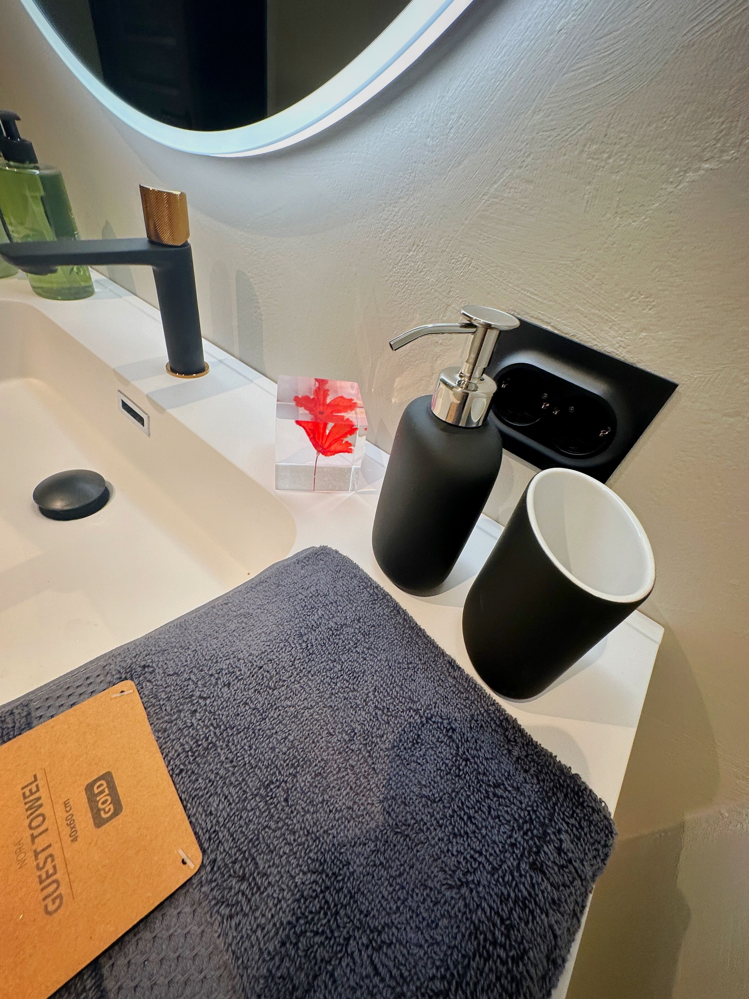 Une salle de bain avec un lavabo, un miroir, un distributeur de savon noir et une tasse noire.