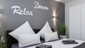 A modern bedroom with a grey accent wall, two white pillows, a bedside table with a plant, and a bed with grey bedding.