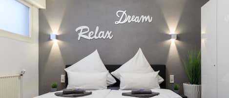 Un dormitorio moderno con una pared gris texturizada, dos almohadas blancas, un cabecero negro y un letrero que dice 'Dream Relax'.