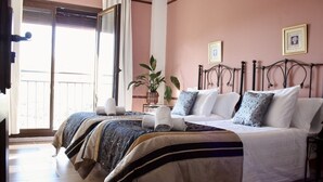A hotel room with a bed, a bedside table, a potted plant, and a window with blinds.