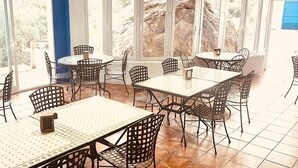 A dining area with tables and chairs, large windows, and a view of rocky terrain.