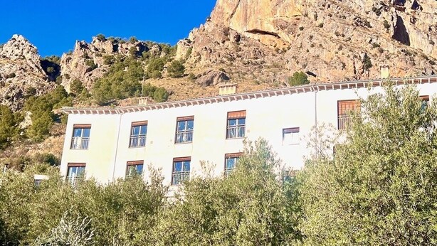 A building with multiple windows and a white facade, set against a rocky hillside.