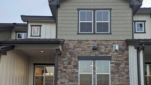 Une maison à deux étages avec une façade en pierre, un patio couvert avec des meubles d’extérieur et une clôture en métal noir.