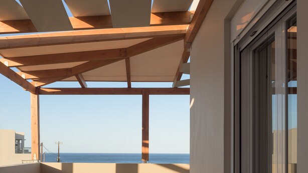 Un balcon avec vue sur la mer, des poutres en bois, une table avec des oranges et deux chaises.