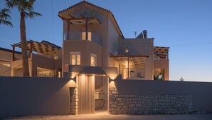 Une maison moderne à deux étages, dotée d’un balcon, d’un mur en pierre et d’un palmier.