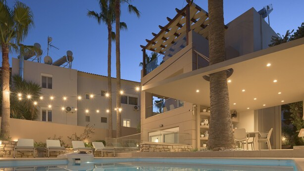 A modern poolside area with lounge chairs, a pool, and a multi-story building with outdoor seating.