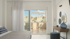 A hotel room with a bed, a small table, a chair, a balcony with an umbrella, and a view of the outside.