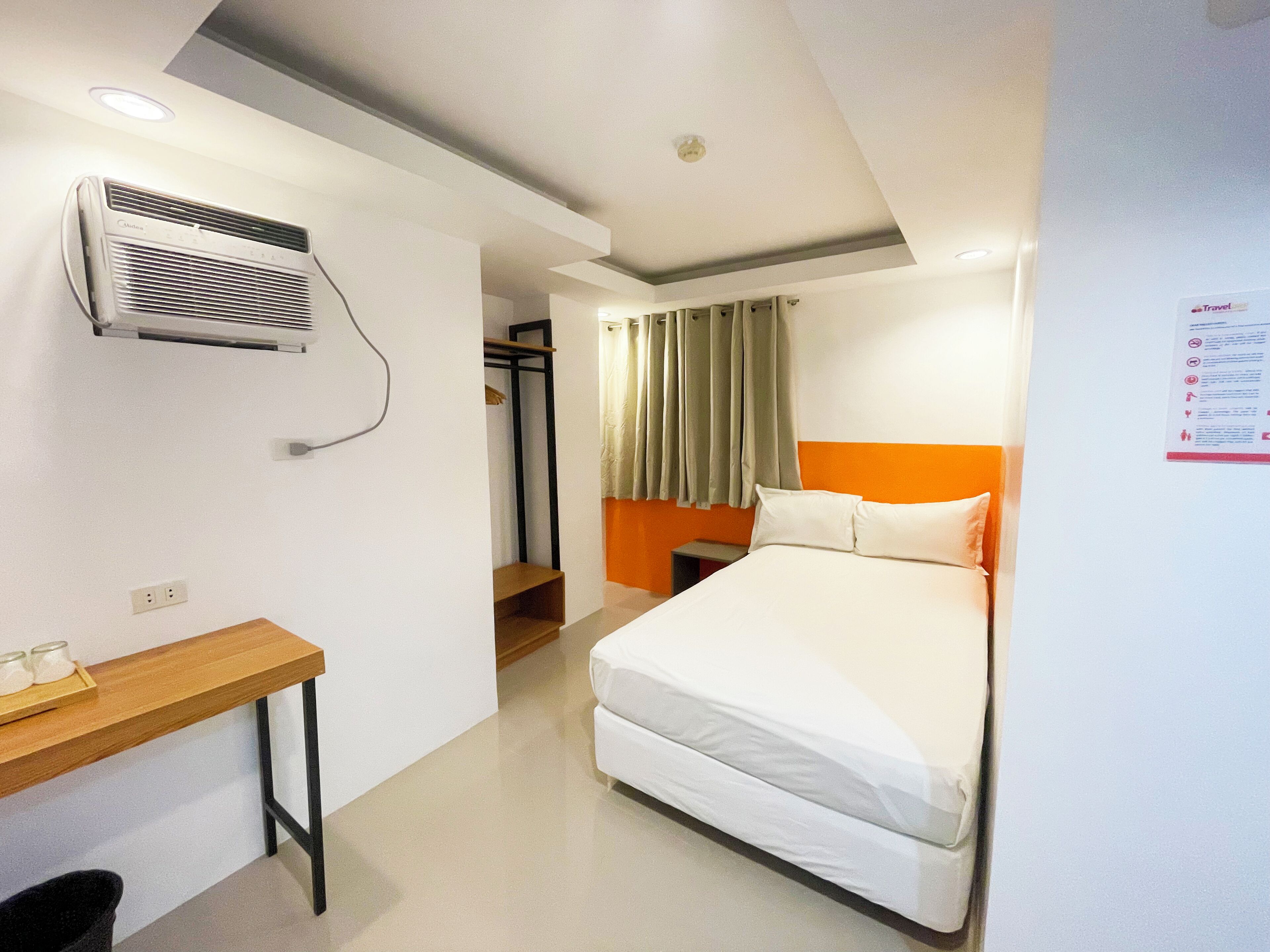 A hotel room with a bed, a desk, an air conditioning unit, and a bathroom visible through an open door.
