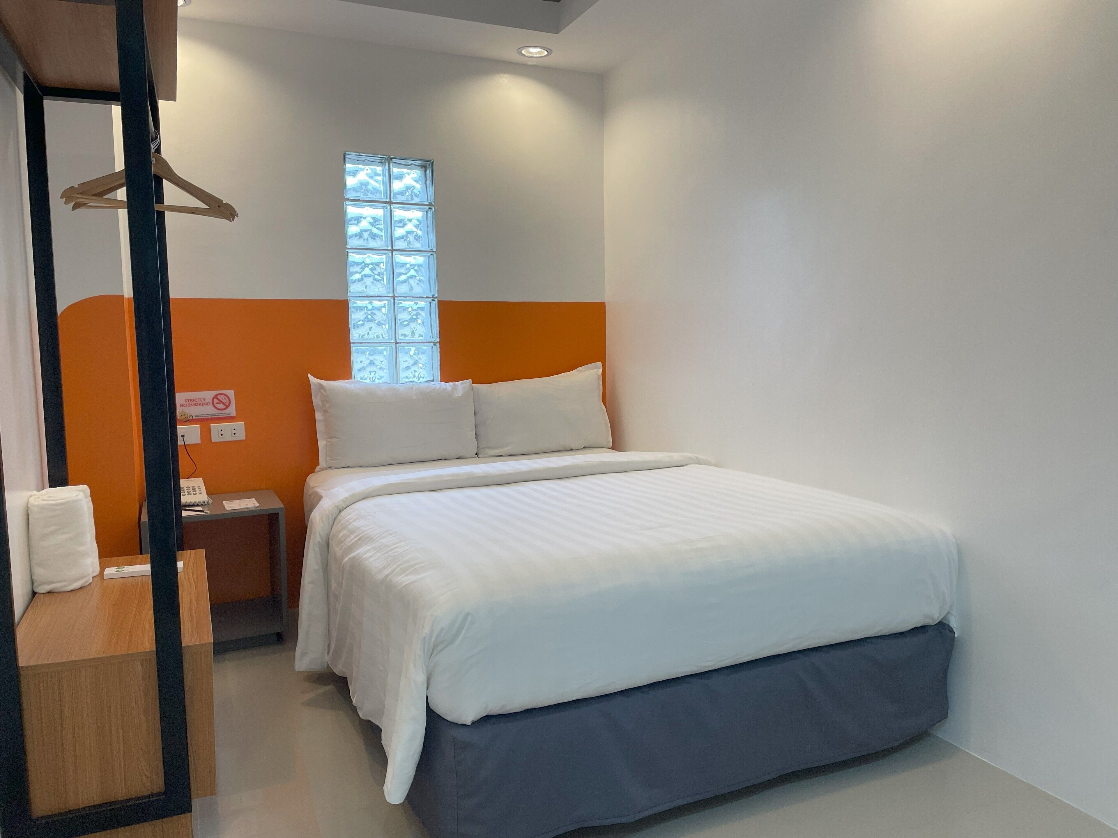 A neatly arranged hotel room with a bed, a bedside table, a hanging coat rack, and a window with a view.