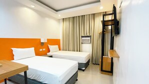 Une chambre d’hôtel avec deux lits, un bureau, un téléviseur fixé au mur et une fenêtre avec des rideaux.
