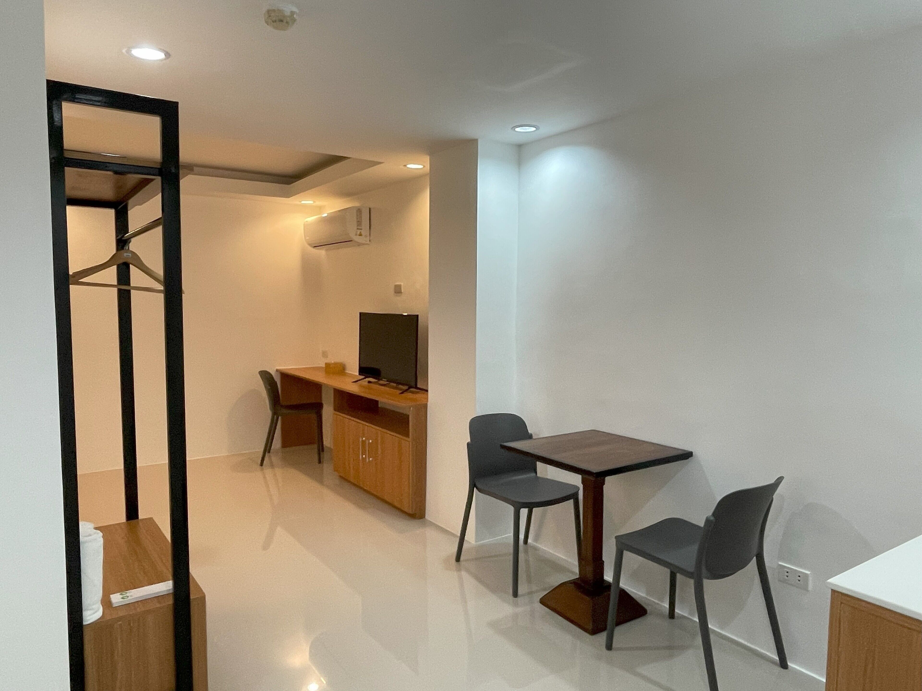 A modern, well-lit room with a wooden desk, two chairs, a television, and a wardrobe.