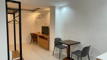 A modern, well-lit room with a wooden desk, two chairs, a television, and a wardrobe.