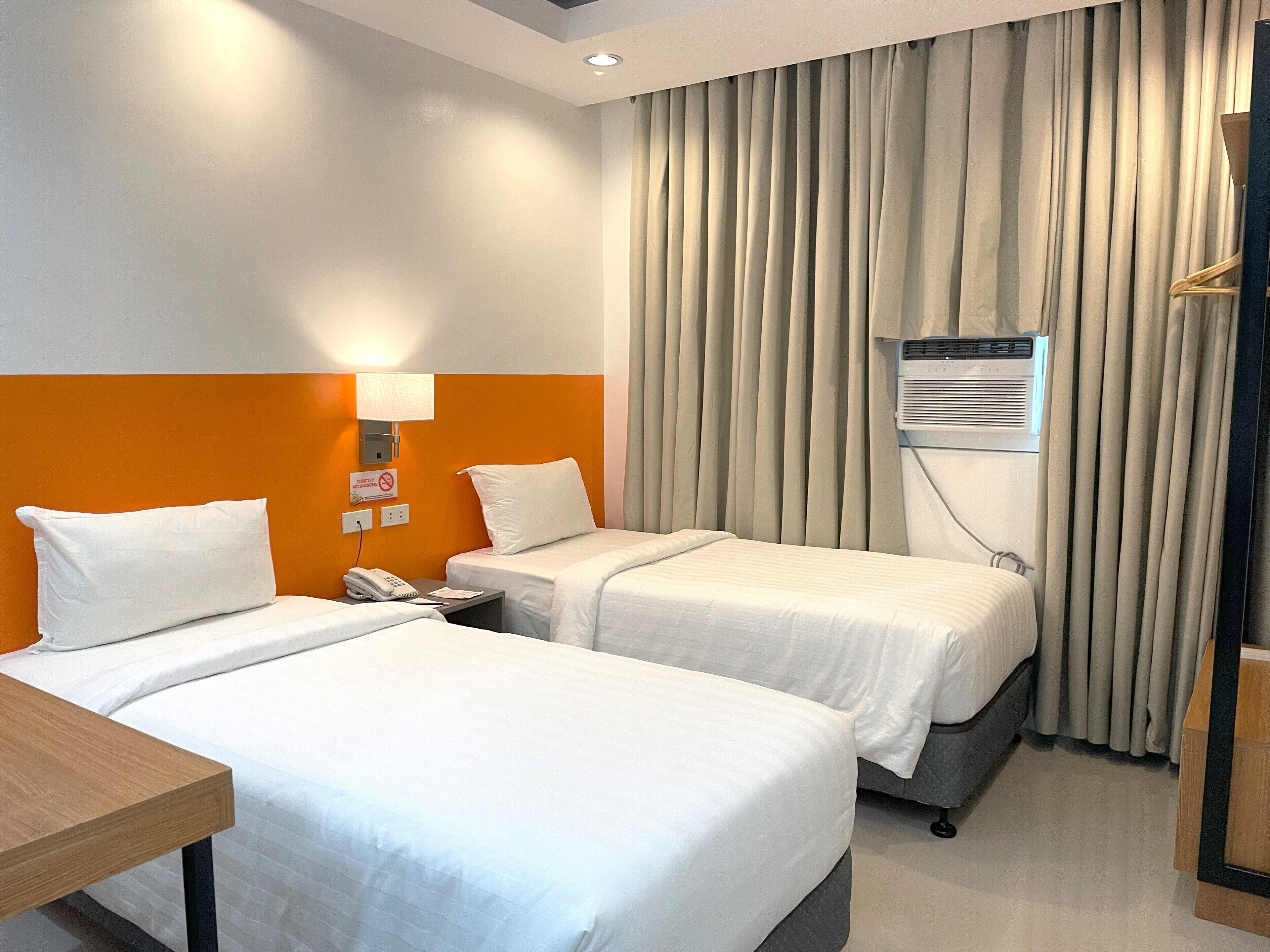 Ein Hotelzimmer mit zwei Einzelbetten, einem Holznachttisch, einem Telefon und einer Klimaanlage.
