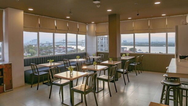 Un espace de restauration moderne avec des tables et des chaises, de grandes fenêtres offrant une vue sur la ville et un plafond haut doté d’un éclairage encastré.