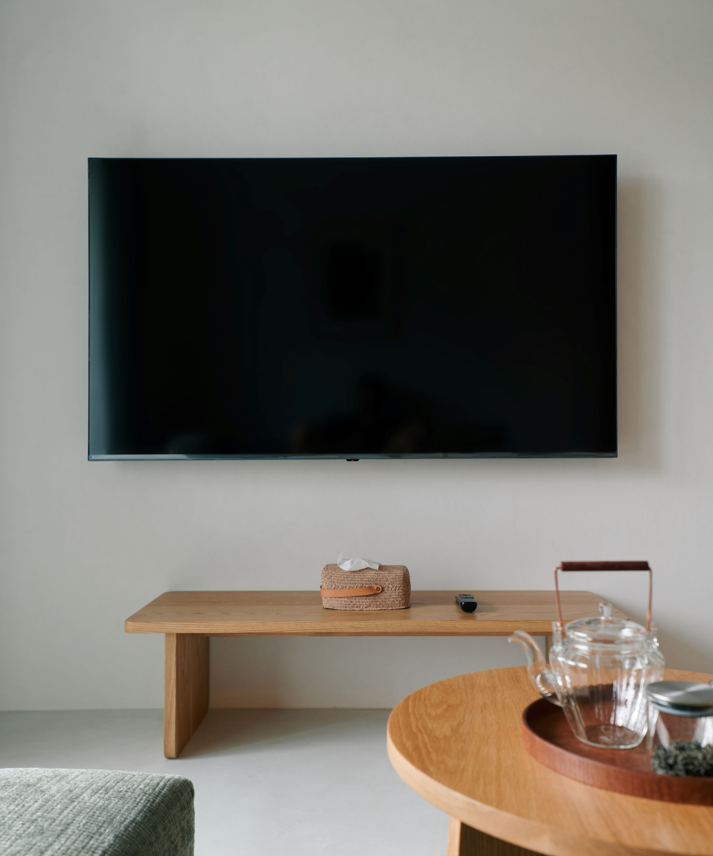 A modern living room with a flat-screen TV mounted on the wall, a wooden bench, and a round coffee table with a glass teapot.