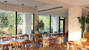 Un comedor amplio con ventanas grandes, mesas y sillas de madera, y una planta en el centro.