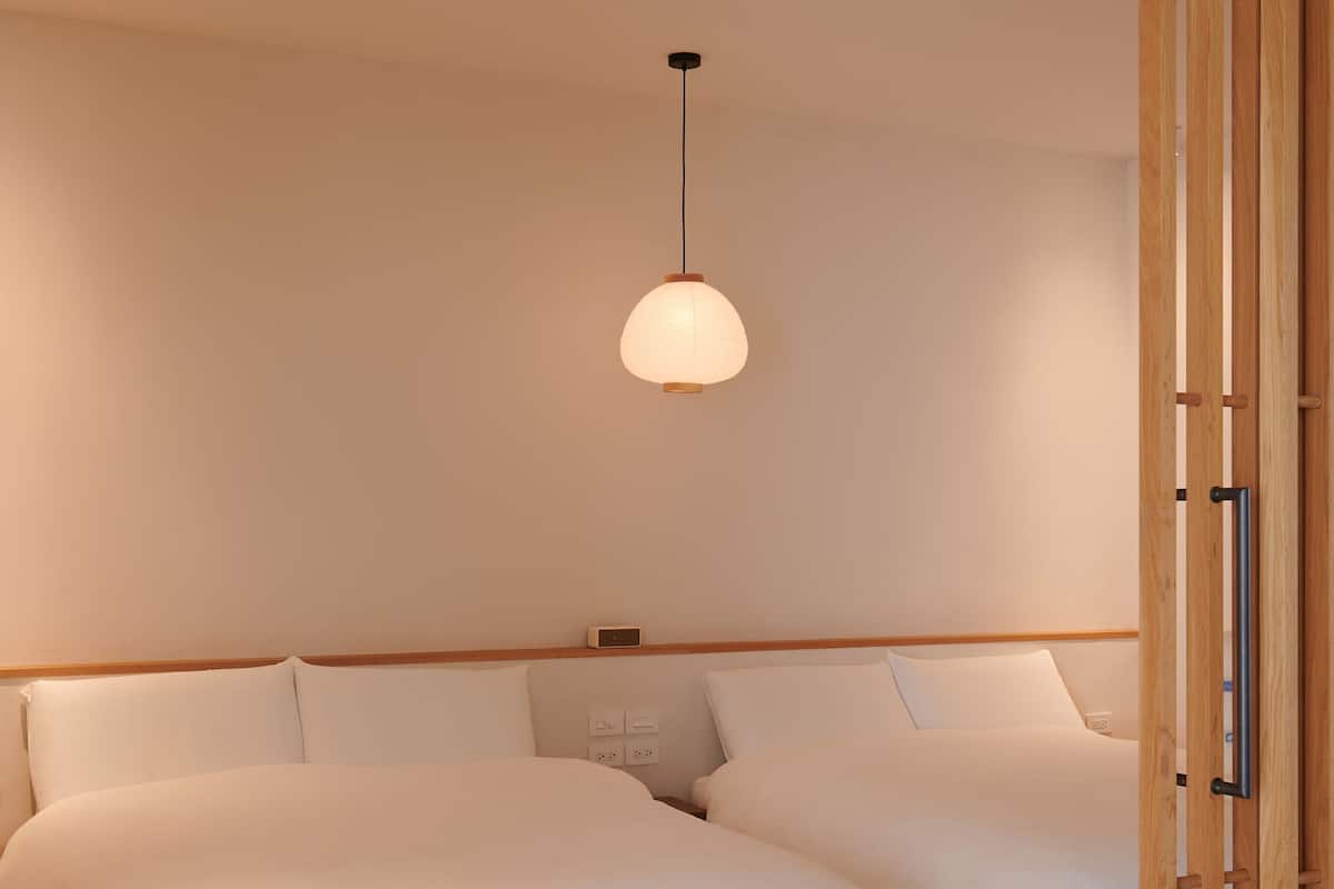 A bedroom with a wooden headboard, a hanging light fixture, and a bedside table with a clock.