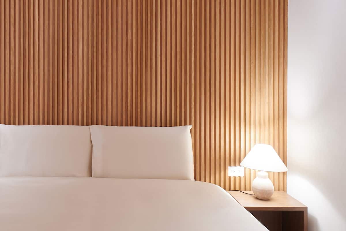 A neatly made bed with white linens, a wooden slatted headboard, and a bedside table with a white lamp.