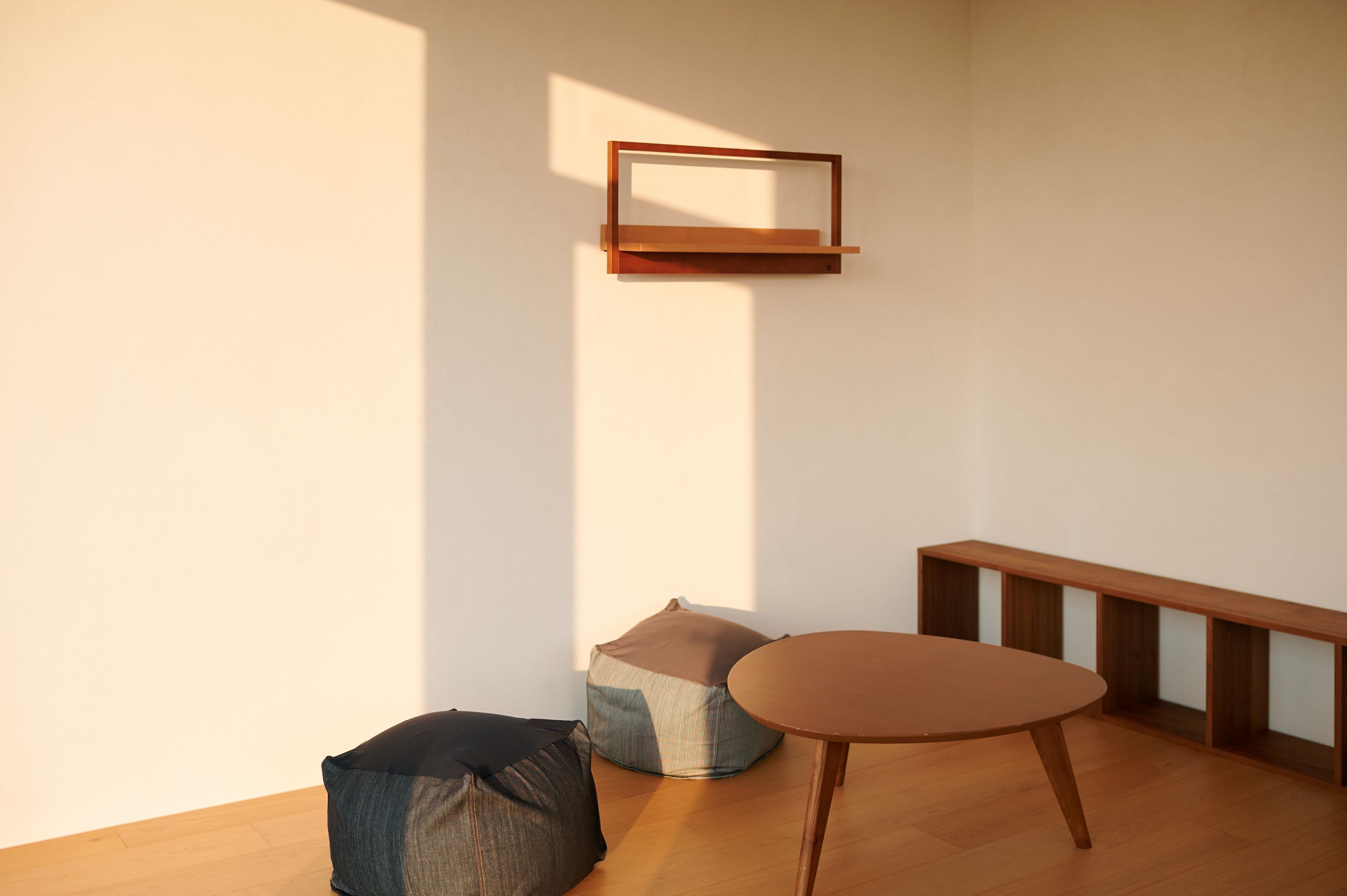 A minimalist room with a wooden floor, a round table, two bean bags, and a wall-mounted shelf.