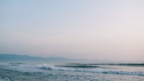 Vista costera con olas y montañas a lo lejos.