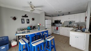 A kitchen with white cabinets, a bar area with blue stools, a ceiling fan, and a coffee-themed wall decoration.