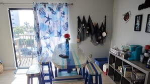 A dining area with a glass table and blue chairs, a ceiling fan, and a view of the outside.
